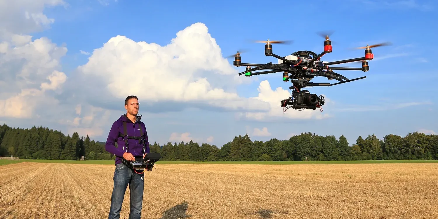 Männliche Person mit Fernsteuerung neben fliegender Kameradrohne (Oktokopter) und einer Canon 5D DSLR Kamera im Gimbal