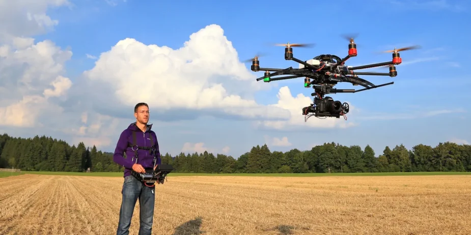 Männliche Person mit Fernsteuerung neben fliegender Kameradrohne (Oktokopter) und einer Canon 5D DSLR Kamera im Gimbal