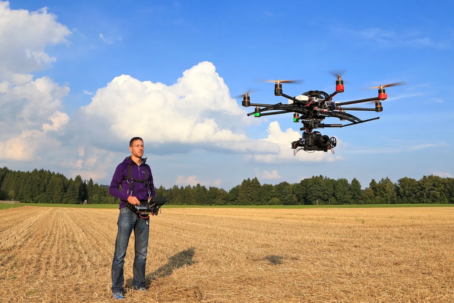 Männliche Person mit Fernsteuerung neben fliegender Kameradrohne (Oktokopter) und einer Canon 5D DSLR Kamera im Gimbal
